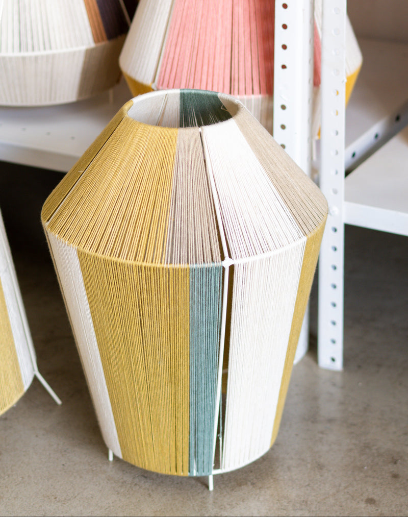 Colorful cylindrical lampshades on a concrete floor with metal shelves in the background.